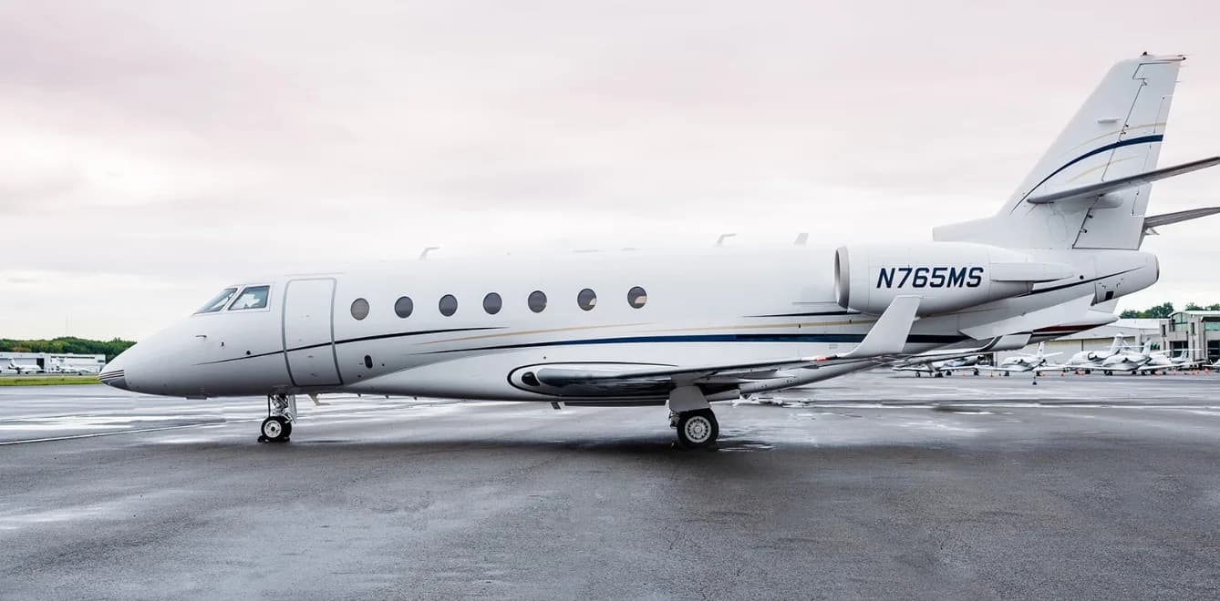 Side view of a white aircraft with blue and gold accents, registration N765MS, parked on the tarmac.