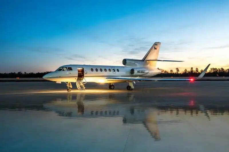 A Falcon jet sits on the tarmac with the door open.