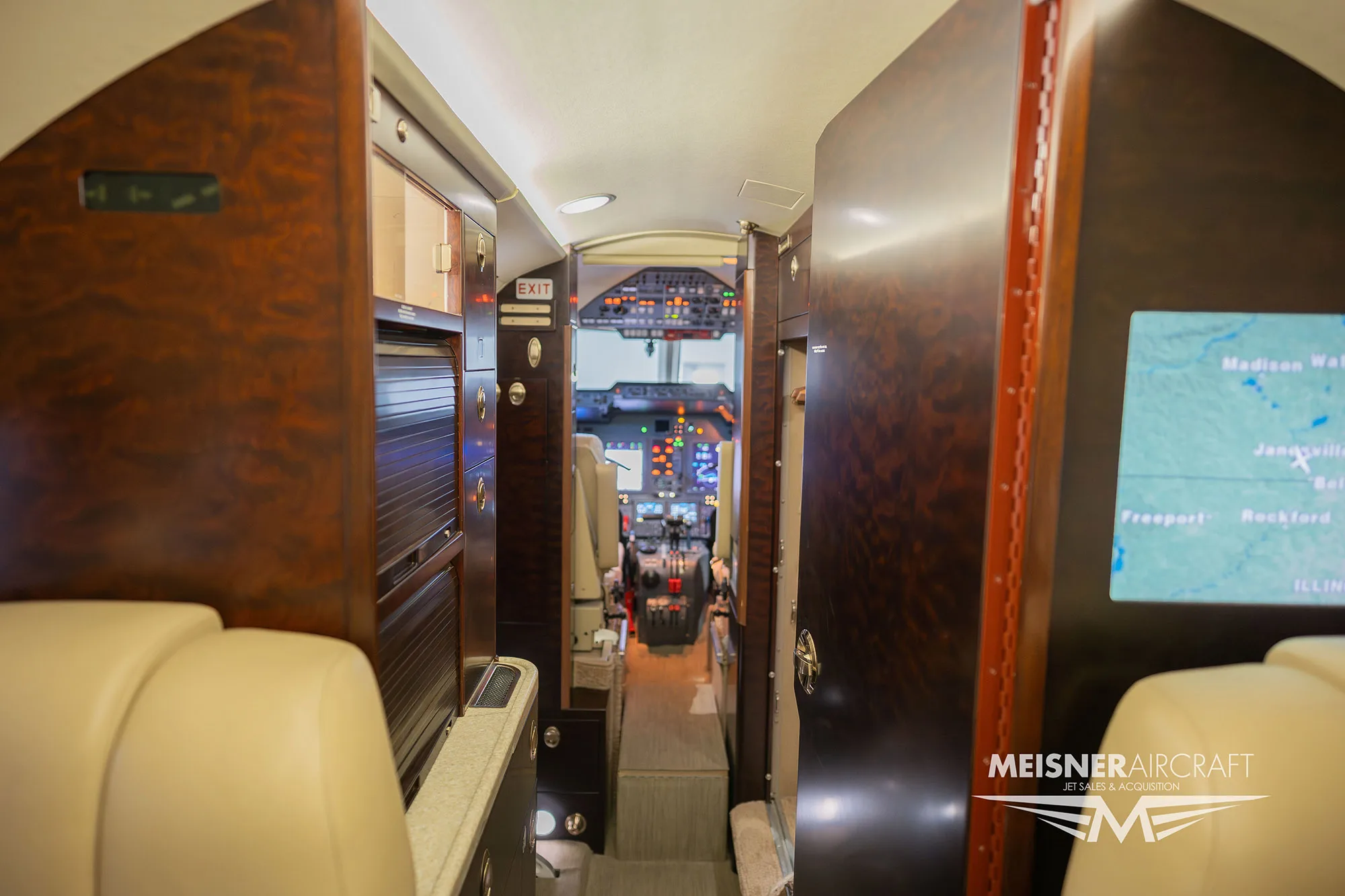 A view from the rear of the business jet cabin, looking forward towards the cockpit, showing galley and cabin details.