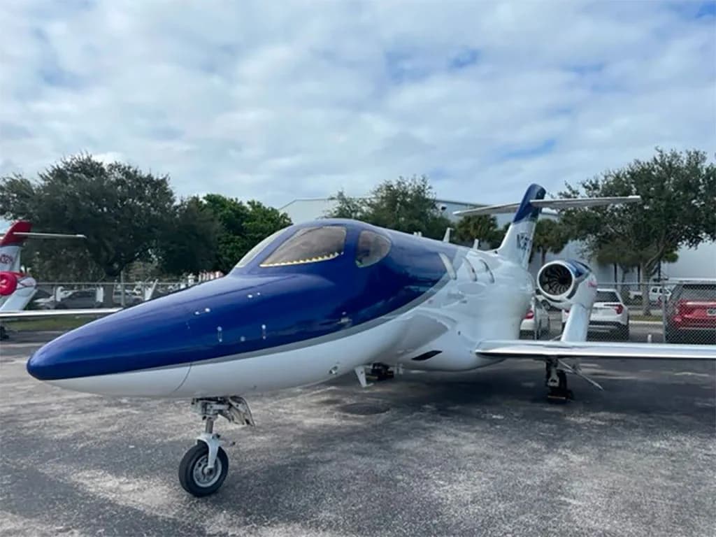 A HondaJet HA-420 with a blue and white paint scheme parked on an asphalt tarmac under a cloudy sky.