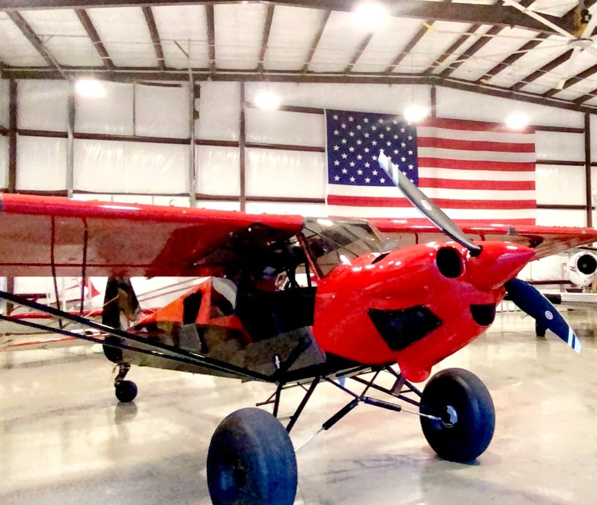 Front view of the red and black N83ZC aircraft in a hangar with an American flag in the background.