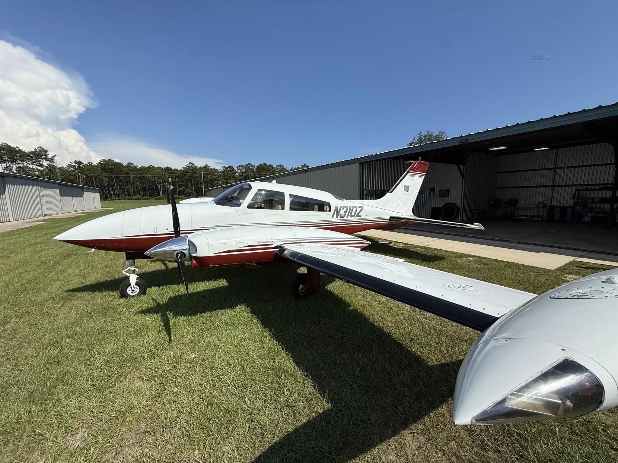 Front-left view of a white and red twin-engine aircraft (N310Z) parked on grass next to a hangar.