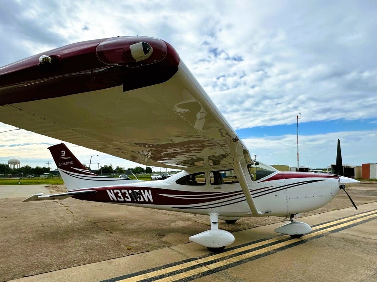 A white and maroon Cessna 182 Skylane (N331GW) is parked on an asphalt tarmac under a partly cloudy sky, viewed from the front-left side.