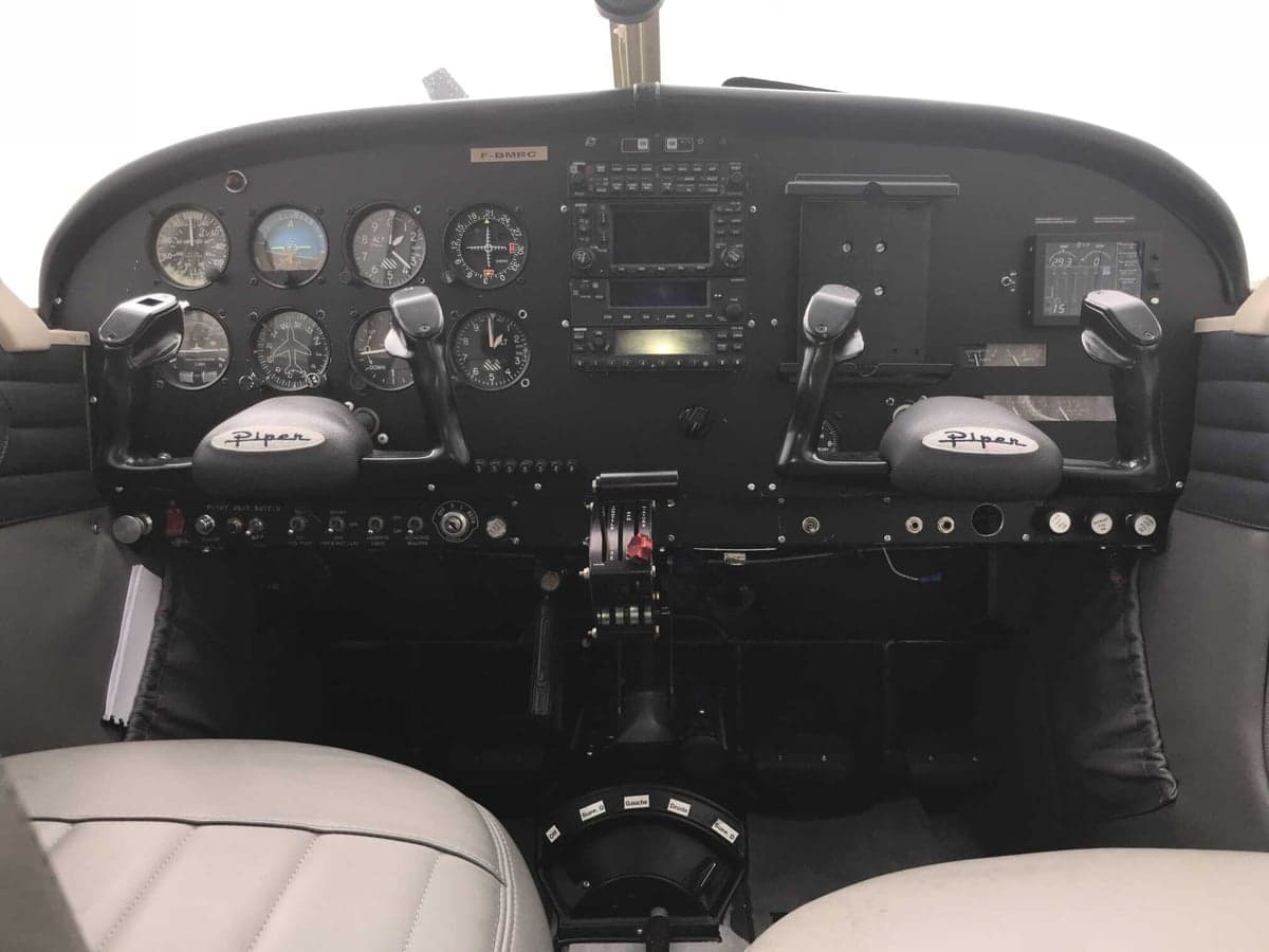Full view of a Piper aircraft cockpit with a black instrument panel and gray seats.