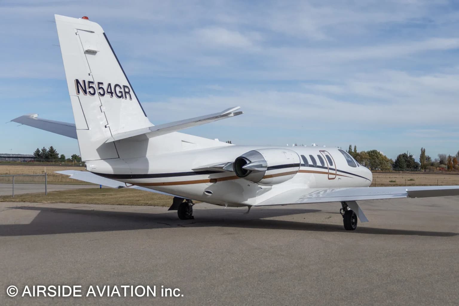 A close-up rear view of a white Cessna Citation business jet with gold and black stripes, registration N554GR.
