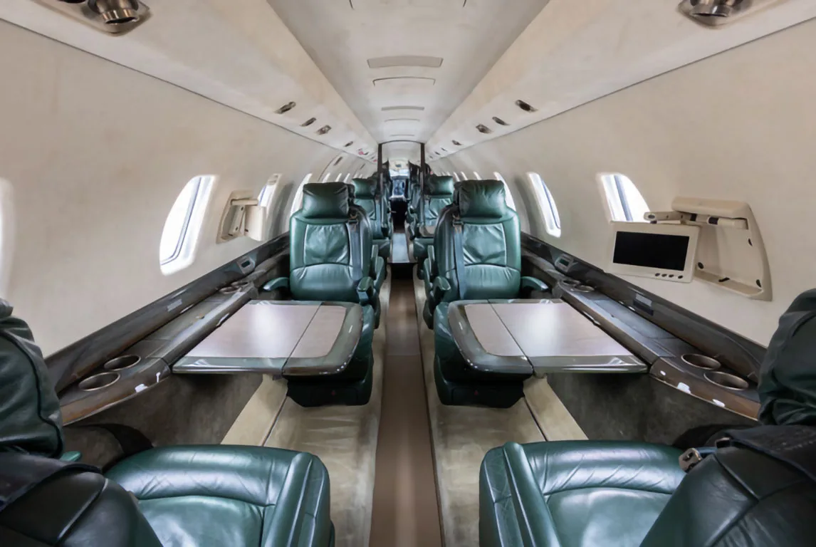 The interior cabin of a private jet with dark green leather seats and tables deployed.