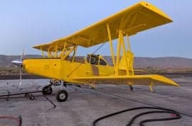 A yellow biplane crop duster sits on the tarmac.