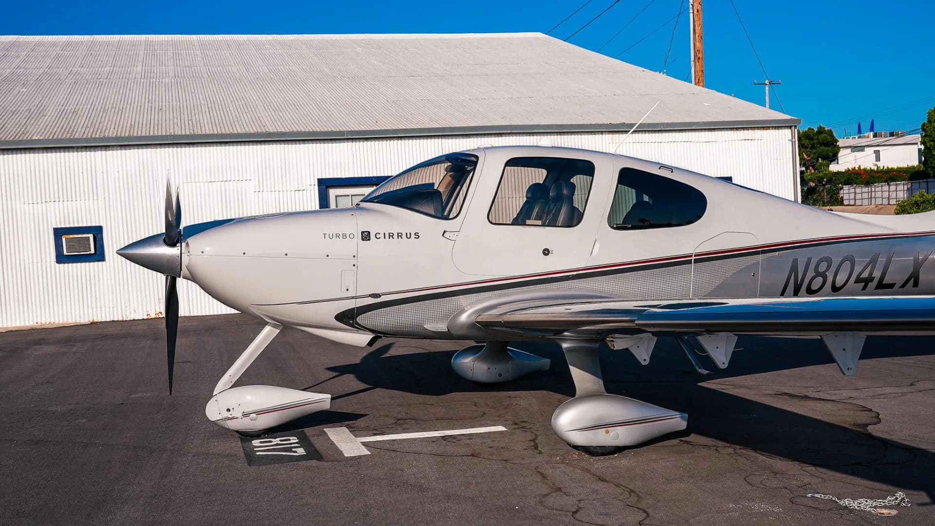 A side view of the white and silver Cirrus SR22T aircraft N804LX parked on an asphalt apron.