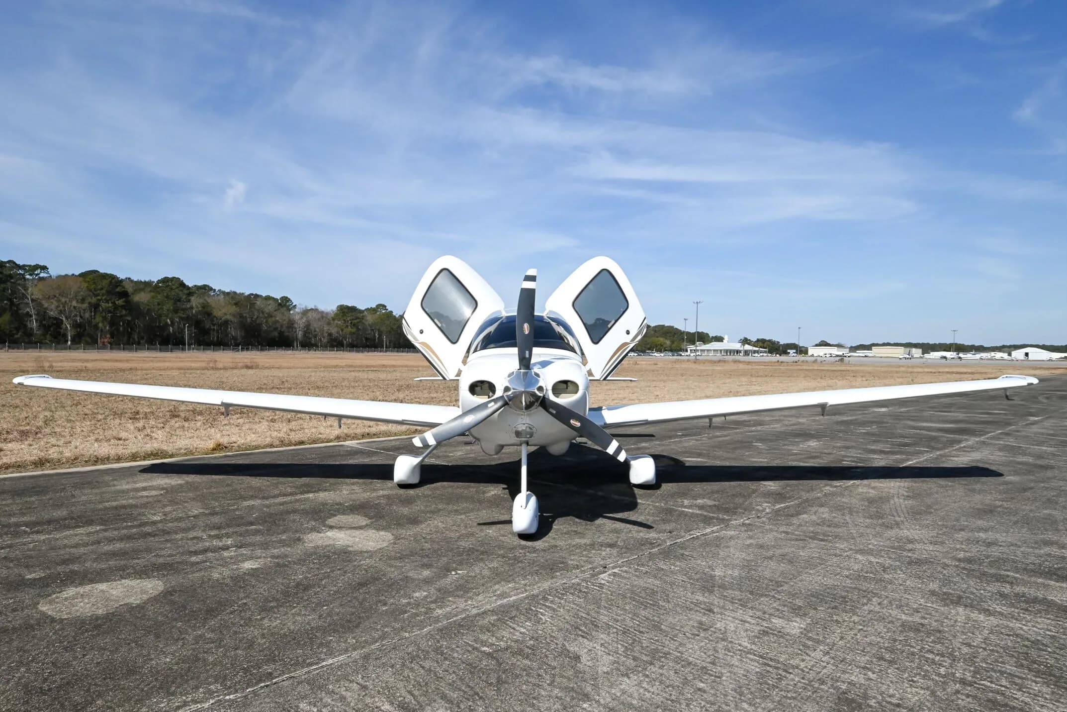 Front view of a white Cirrus SR20 aircraft with its doors open, parked on an airfield.