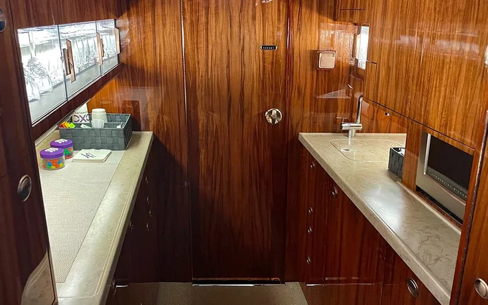 The galley area of a private jet, equipped with a sink, microwave, and ample storage, all finished with polished wood cabinetry.