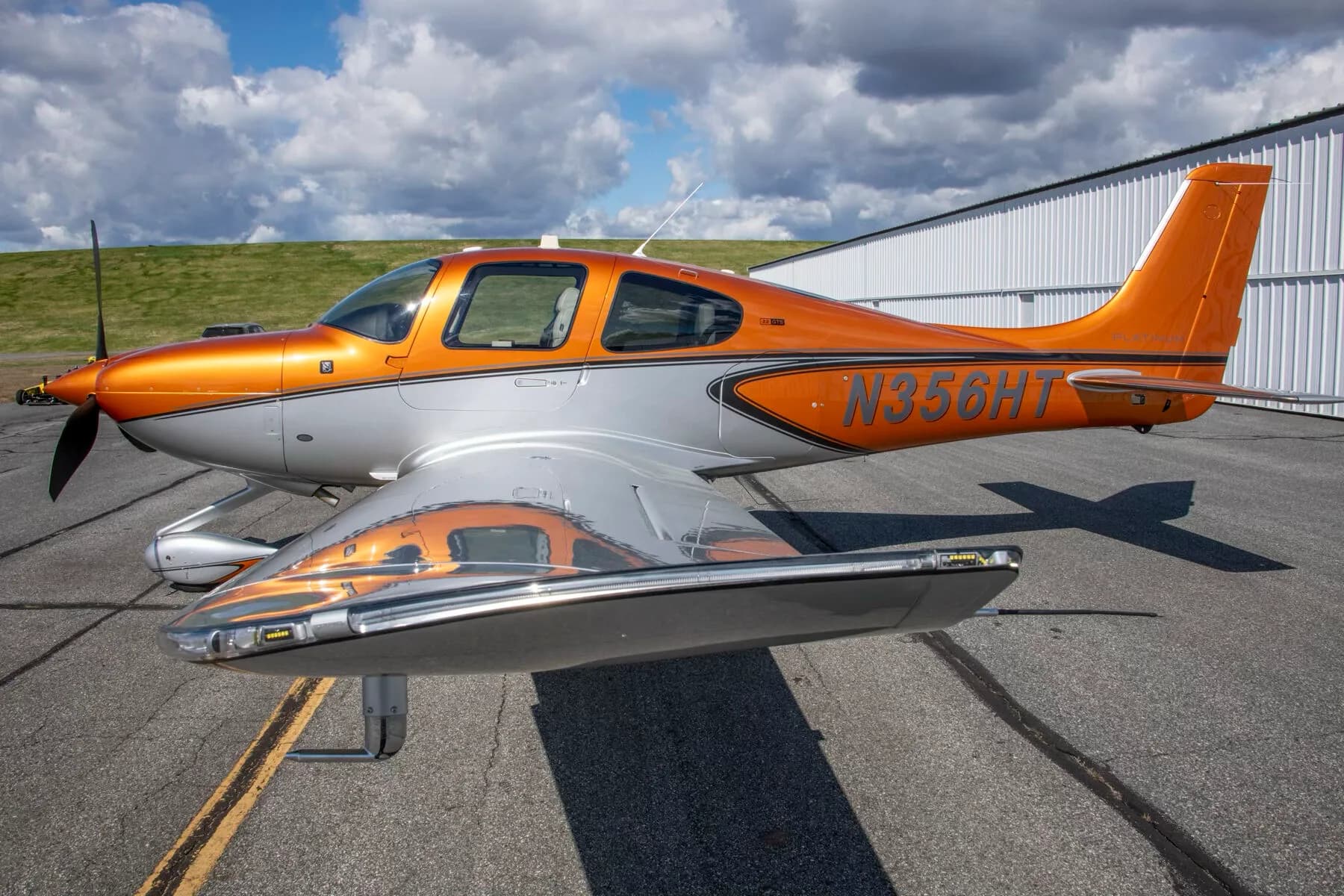 A close side view of a metallic orange and silver Cirrus SR22 aircraft (N356HT) showing reflections on its wing.
