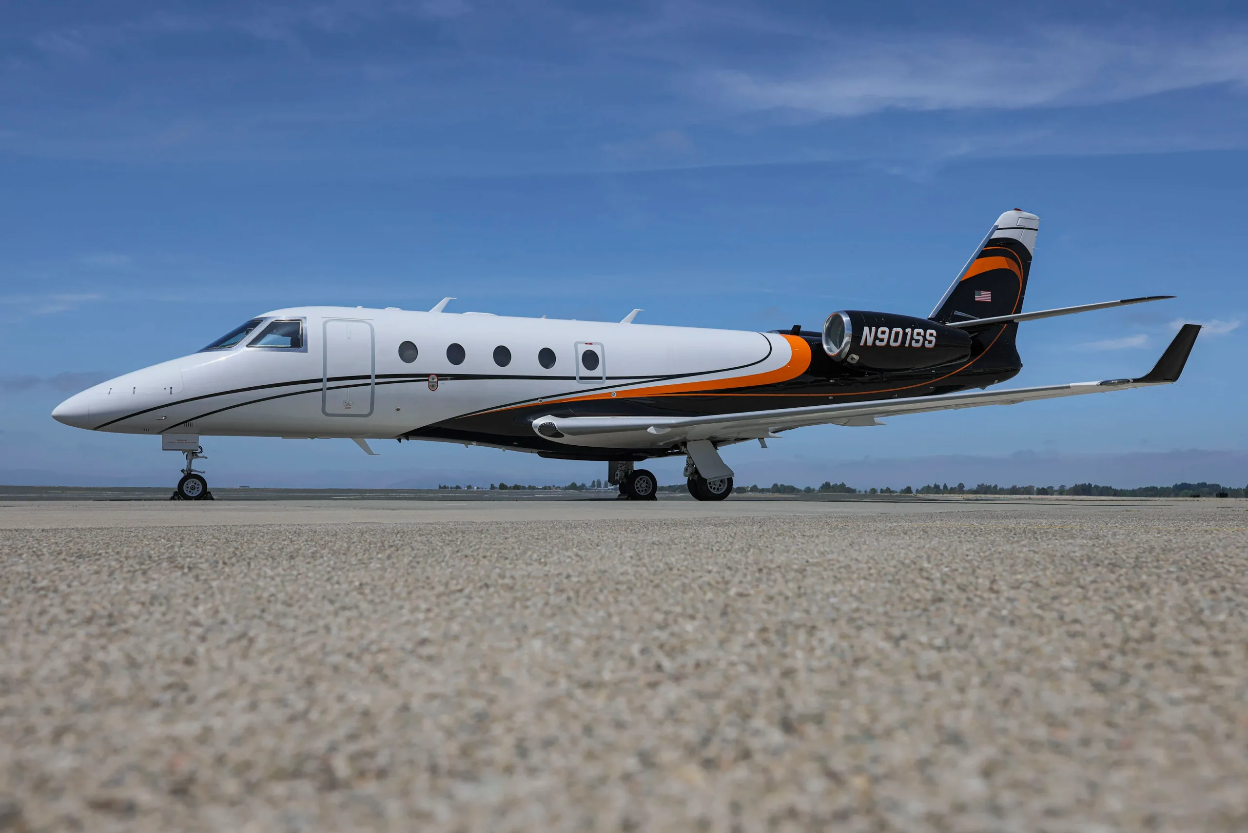 A Gulfstream G280 business jet with a white, black, and orange paint scheme parked on an airfield.