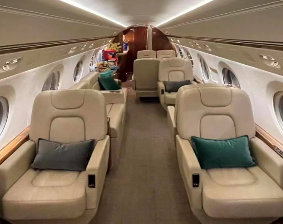 Interior of a private jet with beige leather seats and green pillows.