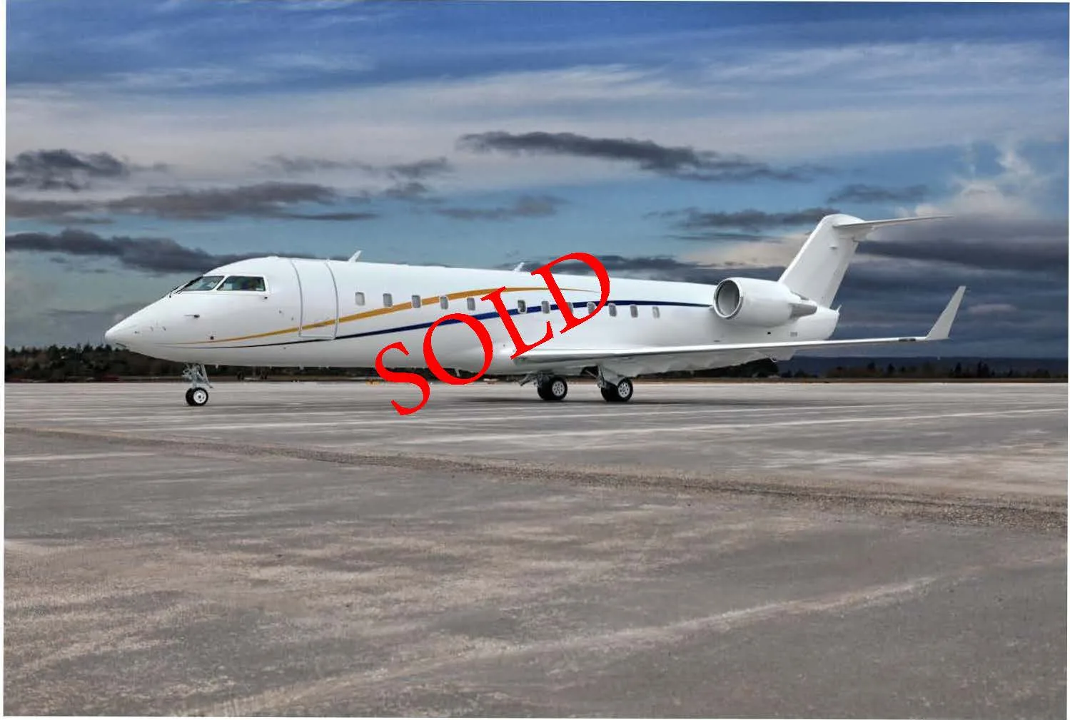 A white business jet with blue and gold stripes on an airfield under a cloudy sky, with 'SOLD' text overlaid.