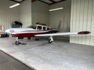 Side view of a maroon and white single-engine aircraft parked in a hangar.