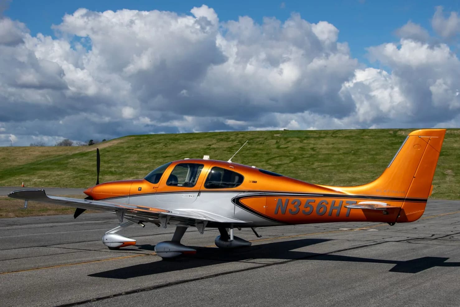 A side view of a metallic orange and silver Cirrus SR22 aircraft (N356HT) parked on an asphalt ramp under a cloudy sky.
