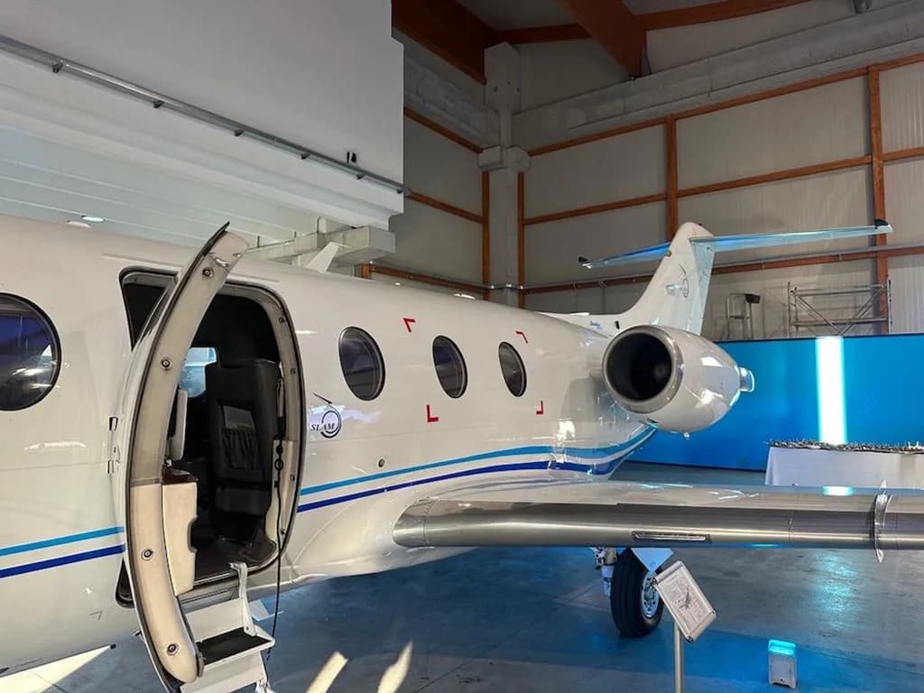 A close-up side view of a white business jet with its main cabin door open, parked in a hangar.
