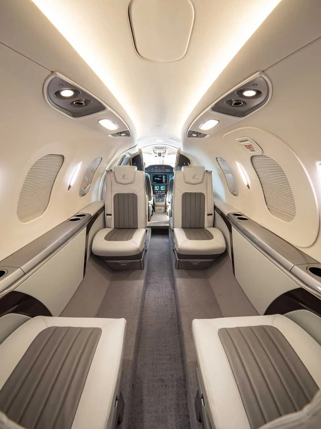 The interior cabin of a HondaJet features light grey and white leather seats, an aisle, and overhead lighting, looking towards the cockpit.