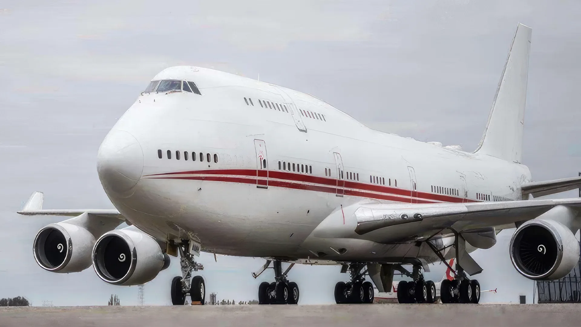 A Boeing 747 with a red stripe on the fuselage is parked on the tarmac.