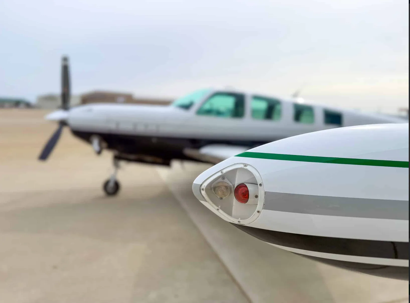 A close-up of the wingtip navigation light of the Beechcraft Baron N157BA, with the aircraft blurred in the background.