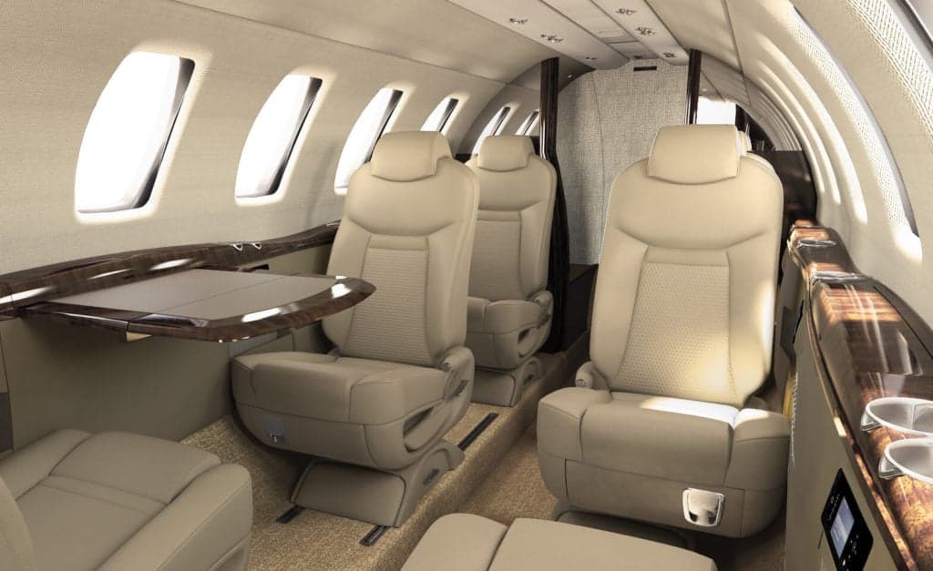 The interior of a Citation CJ4 aircraft with beige leather seats and wood trim.