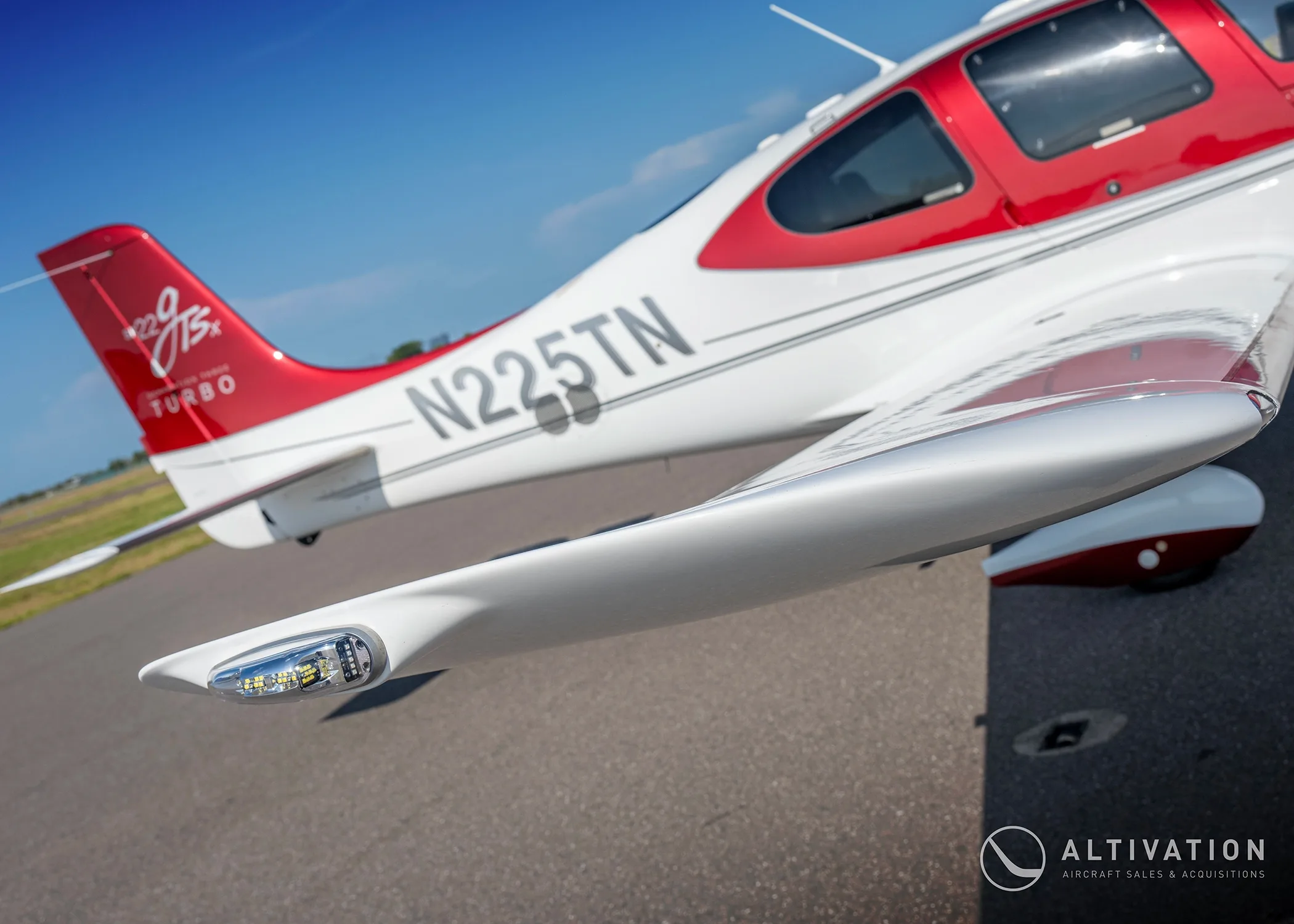 A close-up view of the wingtip and registration N225TN on a red and white Cirrus SR22T aircraft.