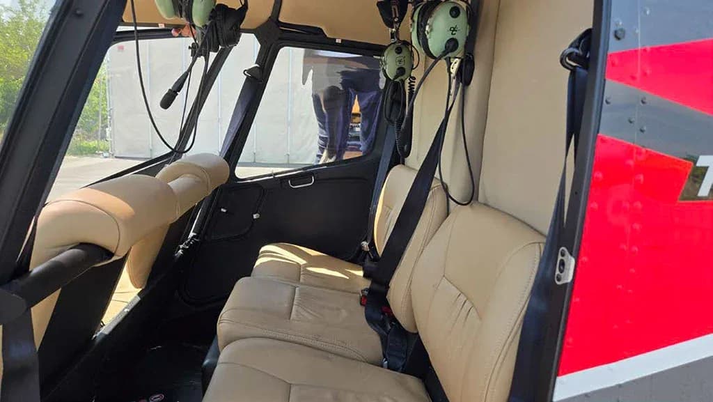 The tan leather interior cabin seats of a helicopter are visible, with headsets hanging near the front.