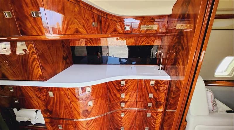 The aircraft's galley features rich, polished wood cabinetry with a white countertop and sink.