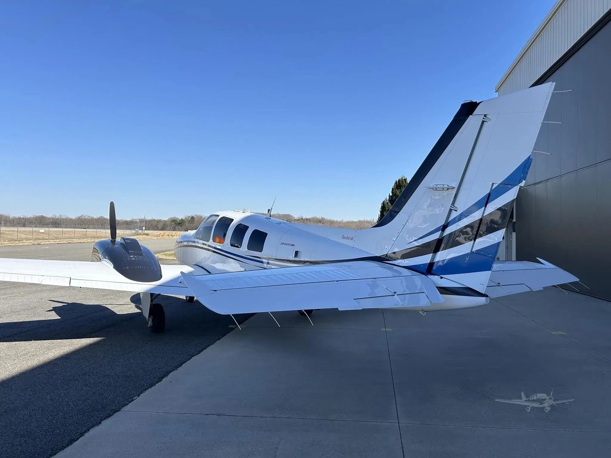 A rear-right view of the white and blue Beechcraft Baron N67WM parked on an tarmac.