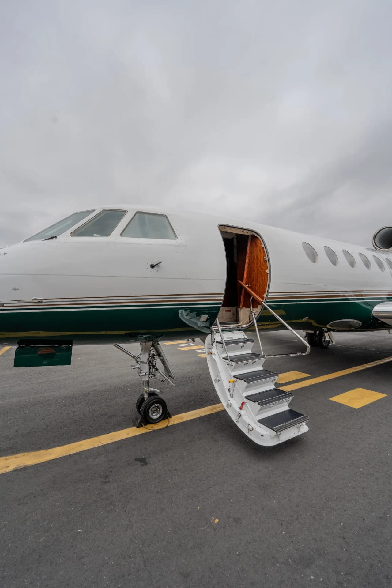The front section of a white and green private jet with its main entry door open and stairs extended.
