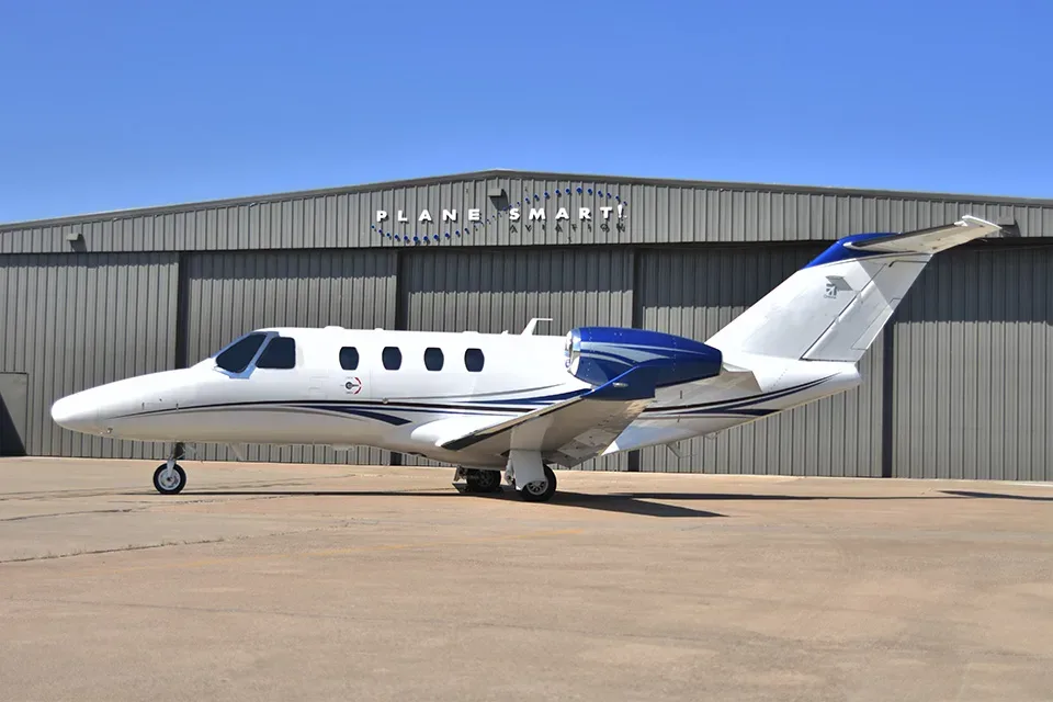 A Cessna Citation jet parked in front of a hangar with the Plane Smart logo.