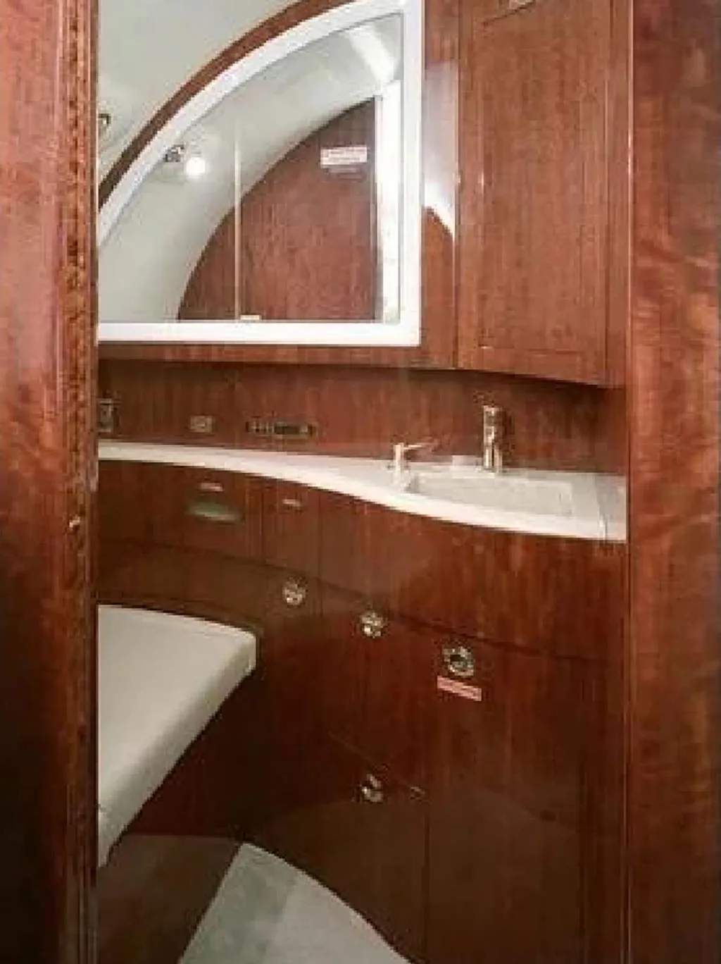 A private jet lavatory with rich wood paneling, a white sink, and a large mirror.