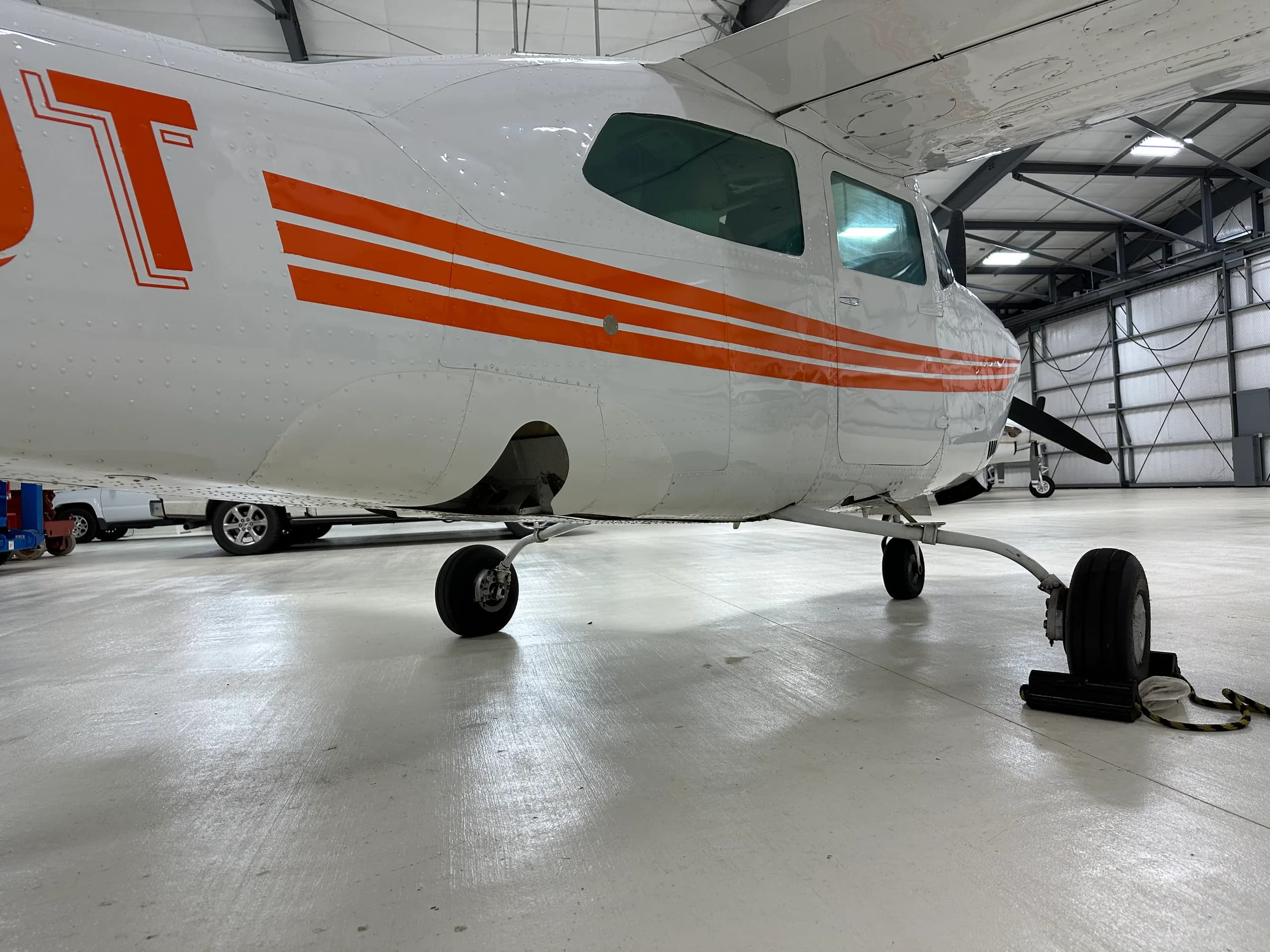 The landing gear and lower fuselage of a Cessna 206 Stationair aircraft with orange stripes.