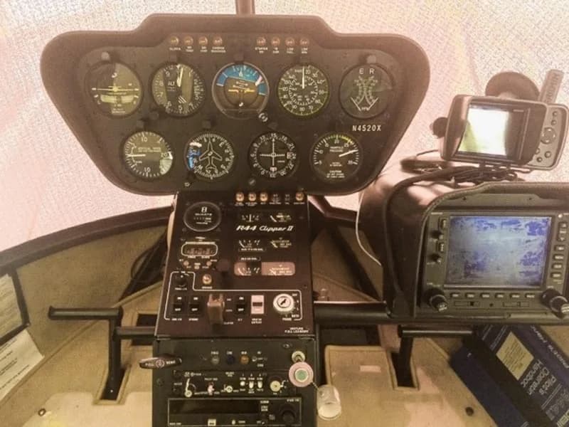 A close-up view of the Robinson R44 Clipper II helicopter's instrument panel, showing gauges, radio controls, and a mounted GPS unit.