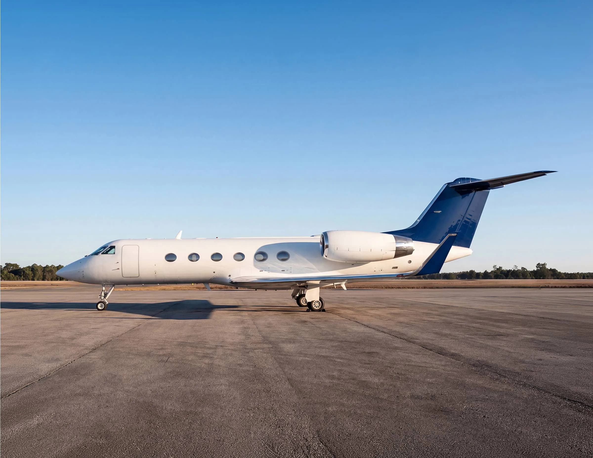 A white business jet with a dark blue tail parked on an airfield under a clear blue sky.