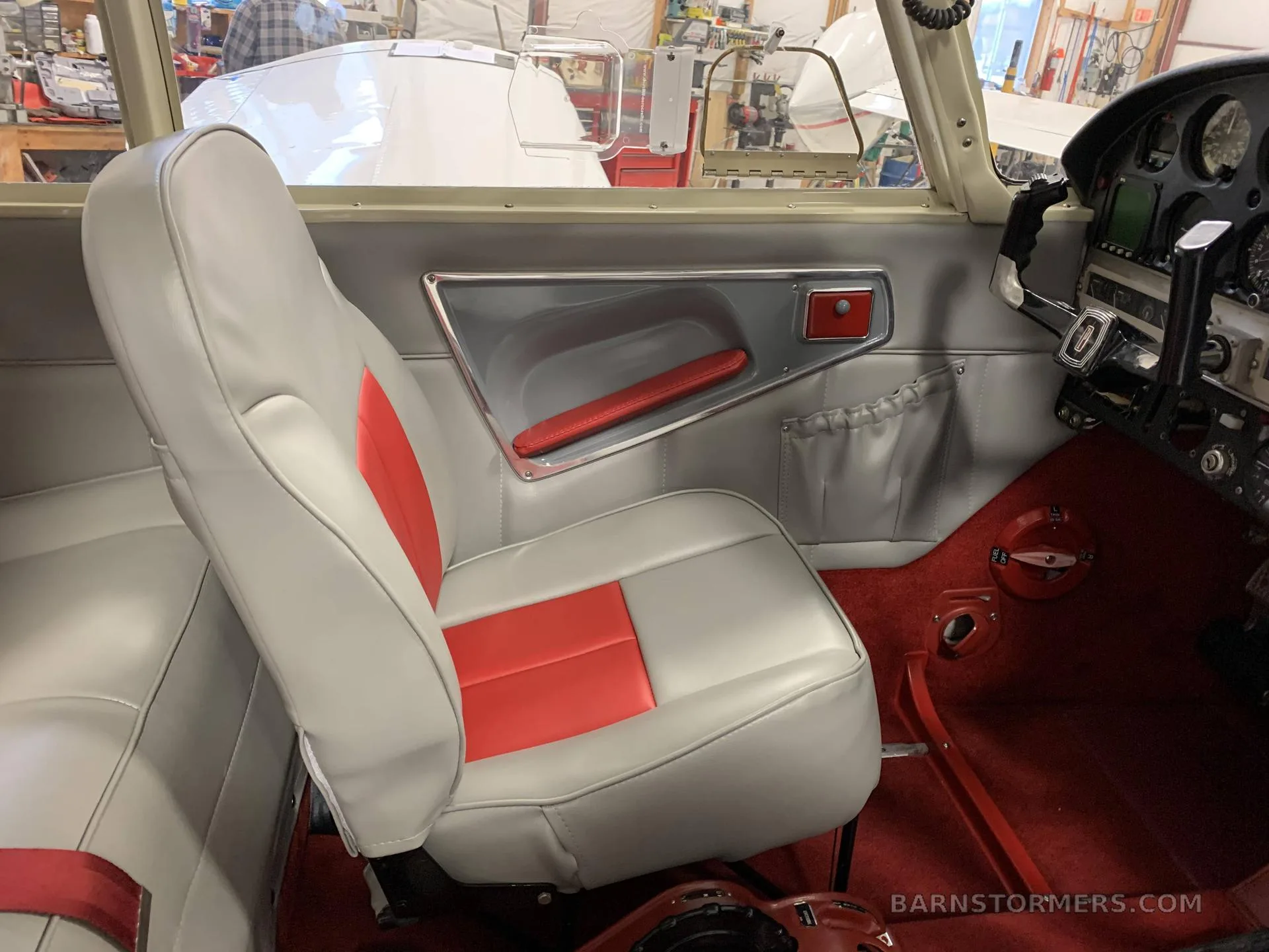 The interior of a Piper Cherokee Arrow, showing a grey and red passenger seat, red carpet, and side panel.