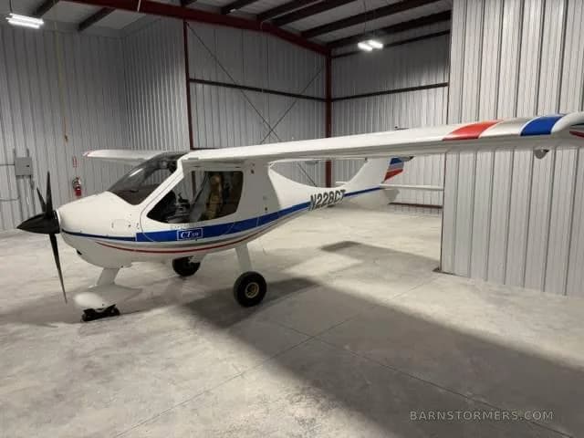 A white CTLS light sport aircraft with blue and red stripes on the tail and wings, parked in a hangar.