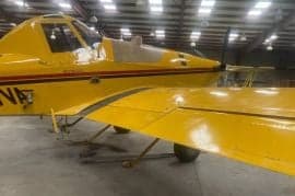 A yellow agricultural aircraft is parked inside a hangar.