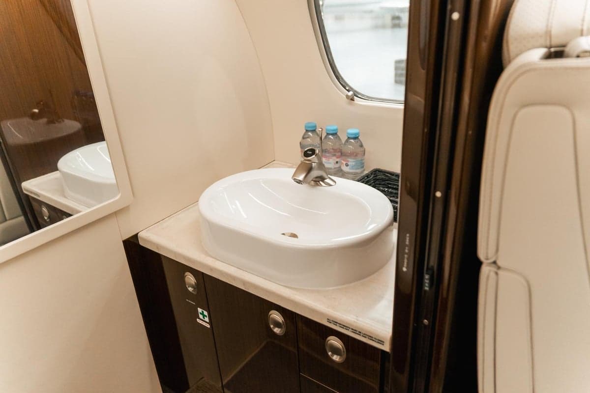 Aircraft cabin interior with cream-colored leather seats, fold-out table, and champagne.