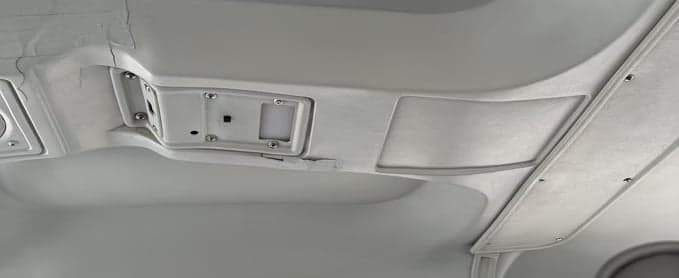 A close-up view of the light grey interior ceiling of an aircraft, showing overhead panels and fixtures.