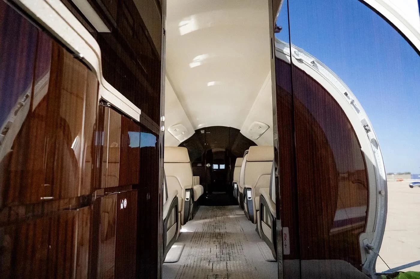 The interior of a business jet viewed from the open main door, showing the aisle and beige seats.