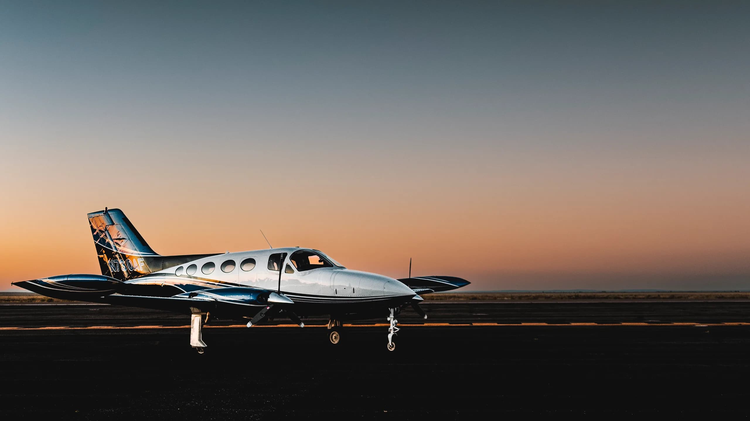 A white and black twin-engine aircraft with its door open on a runway at sunset.