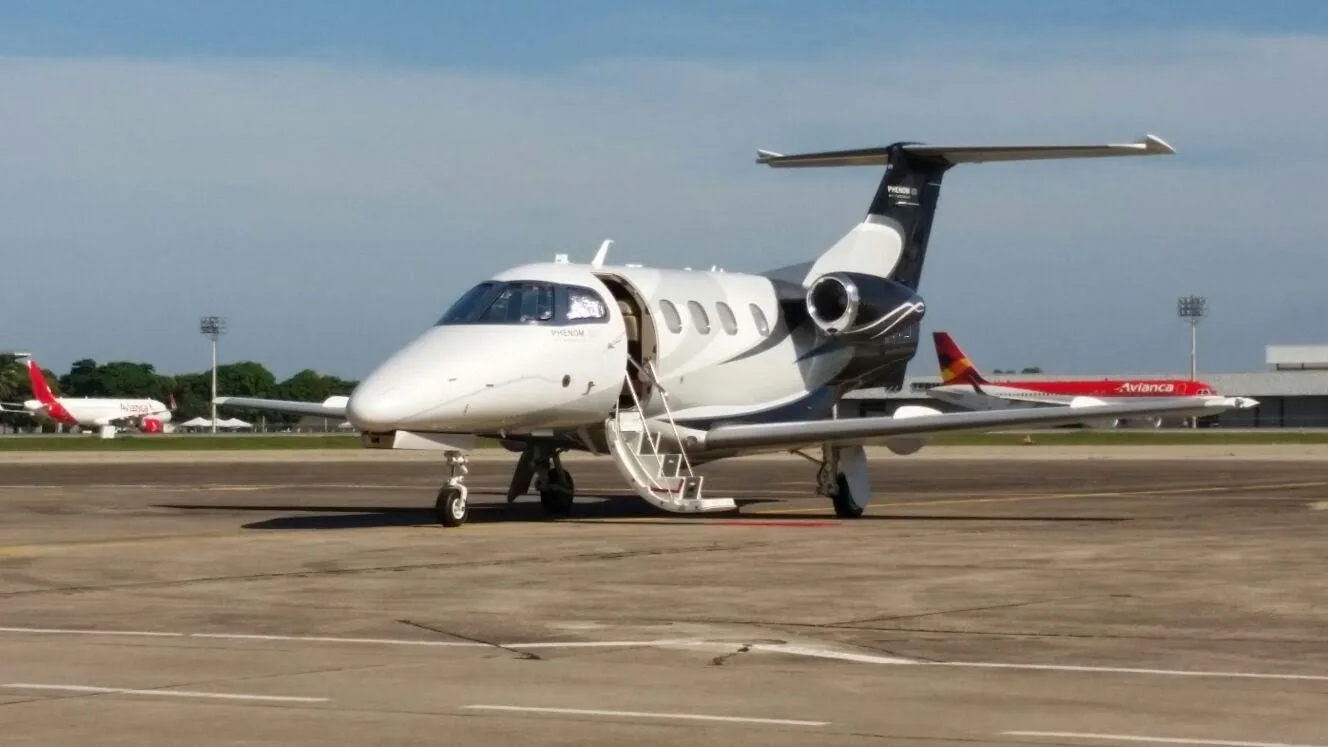 A Phenom 100 aircraft is parked on the tarmac with its door open.