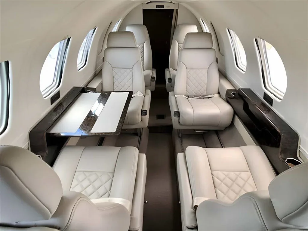 The luxurious cabin interior of a business jet with light-colored leather seats, quilted patterns, and a fold-out table.