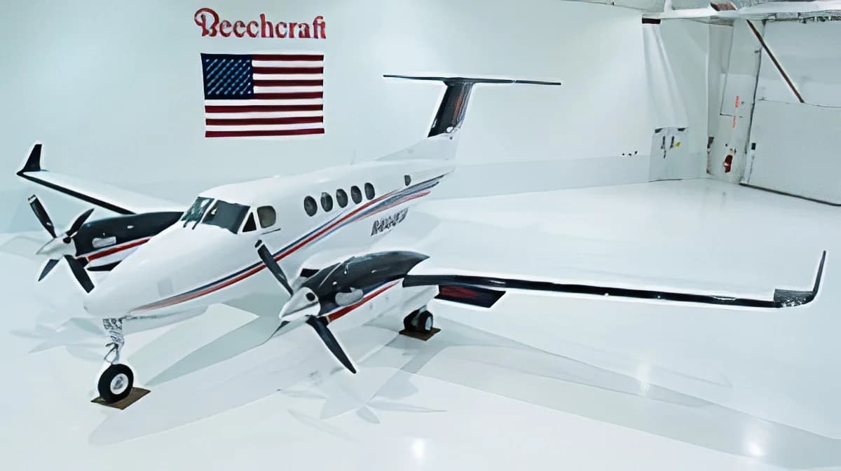 A white Beechcraft King Air twin-turboprop aircraft with black and red accents, parked in a clean white hangar with a Beechcraft logo and American flag on the wall.