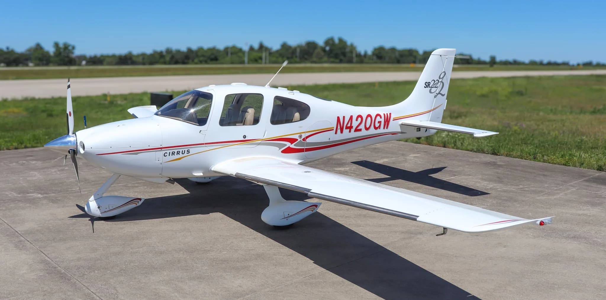 Top-down front-right view of a white Cirrus SR22 aircraft with red and gold stripes on a tarmac.