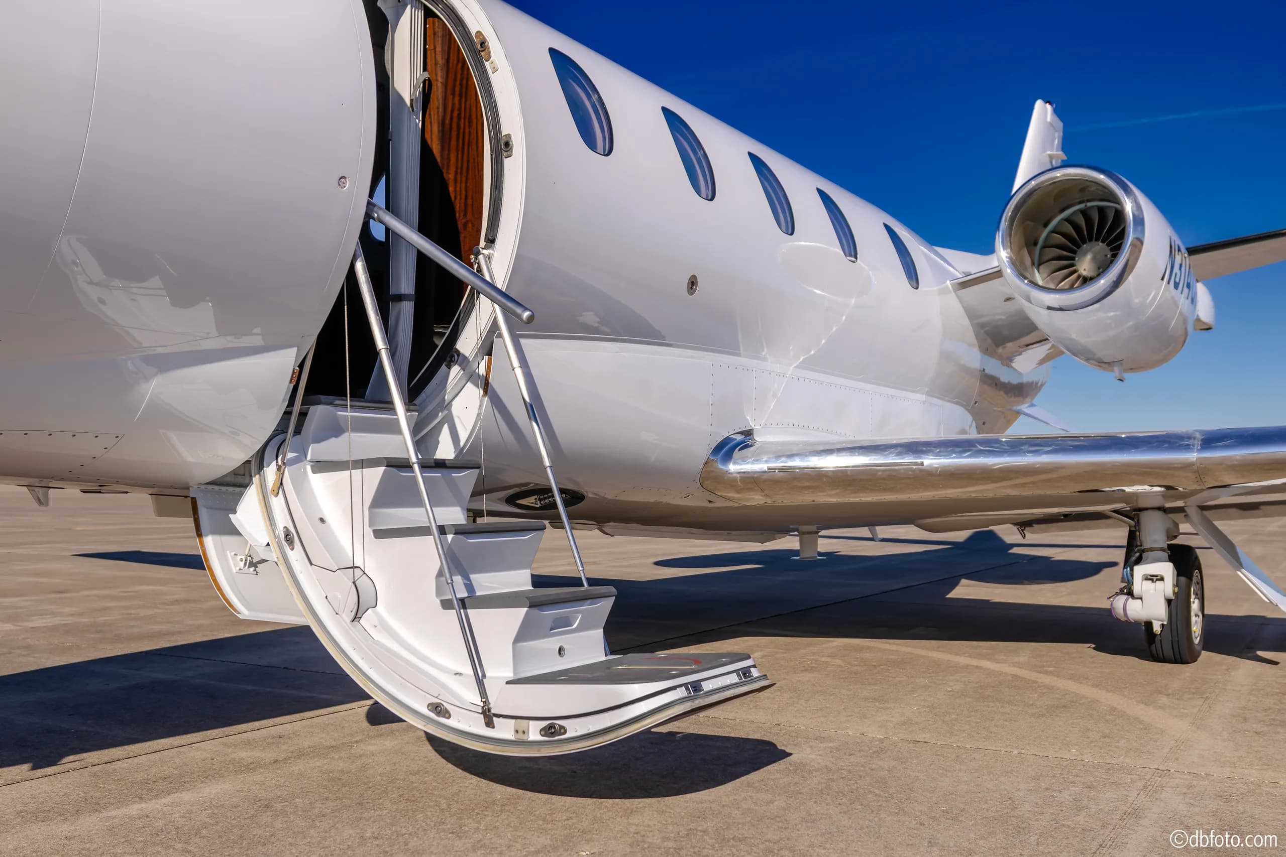 A close-up view of the white business jet's open main cabin door with integrated airstairs extended.