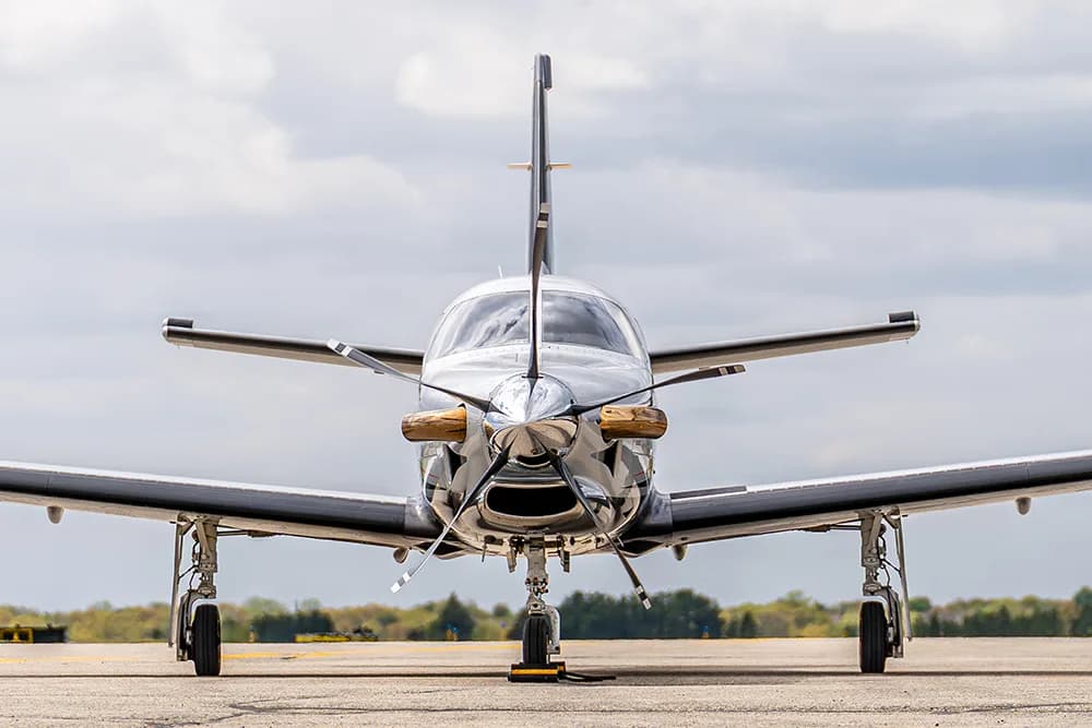 A head-on view of a silver and black TBM turboprop aircraft with its propeller on the tarmac.