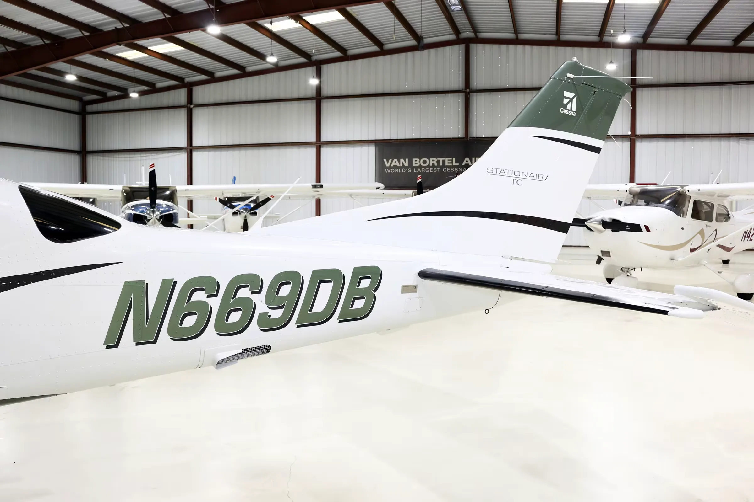 Close-up view of the tail and rear fuselage of a white and green Cessna Stationair TC, registration N669DB, inside a hangar.