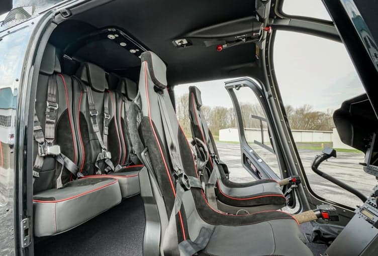 The interior of a helicopter, featuring black leather seats with red accents.